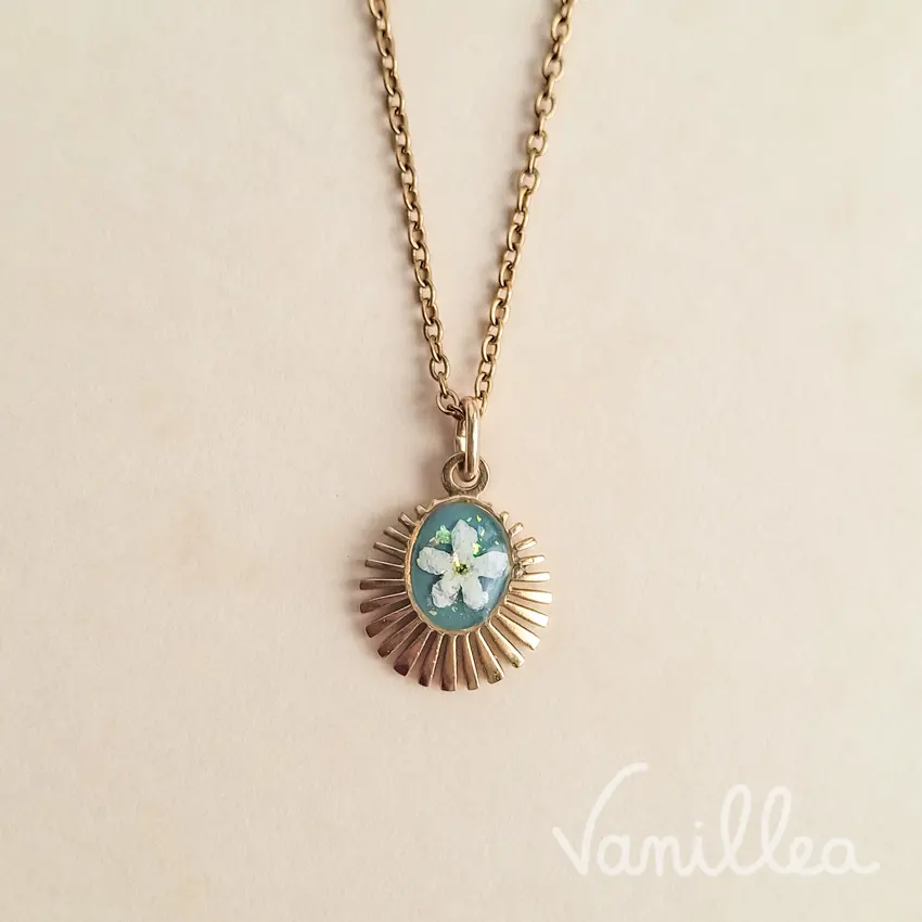 collier médaillon myosotis doré sur fond beige