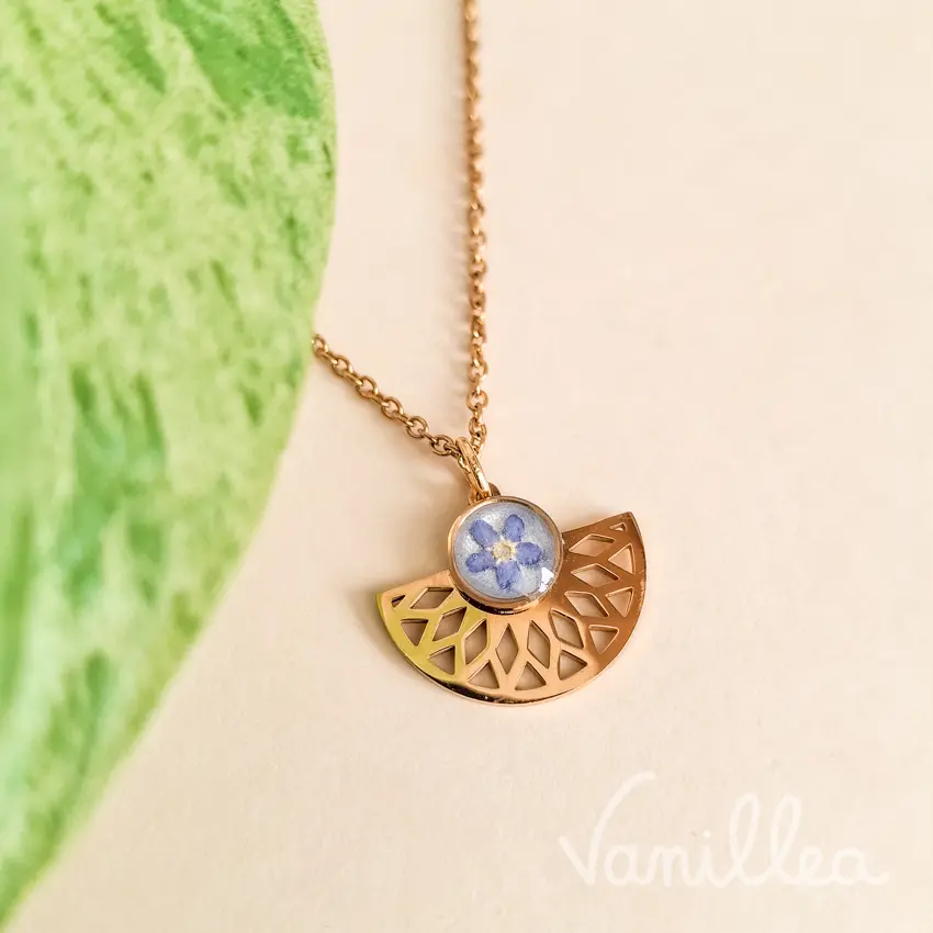 Collier myosotis avec pendentif éventail doré photographié près d'une feuille verte