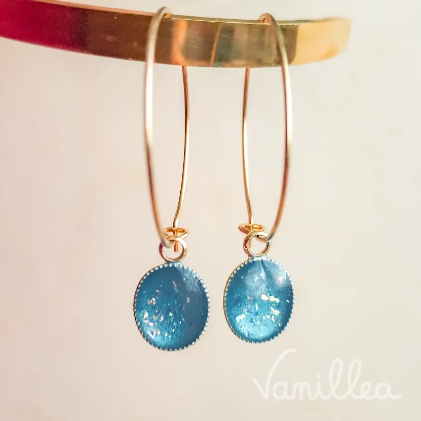 Gros plan sur cabochon bleu azur irisé des créoles dorées pendentif bleu azur