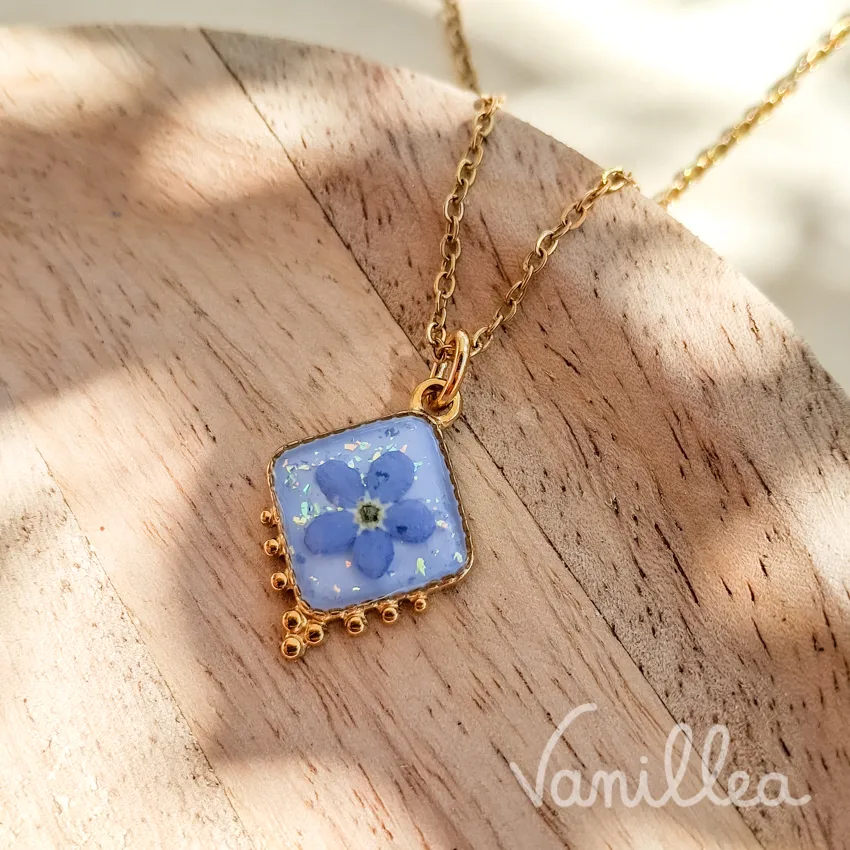 Détail pendentif fleur bleue résine et acier inoxydable doré