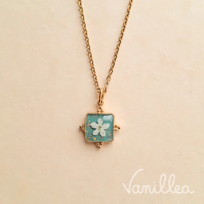 Collier fleur myosotis blanc résine bleu avec pendentif carré doré.