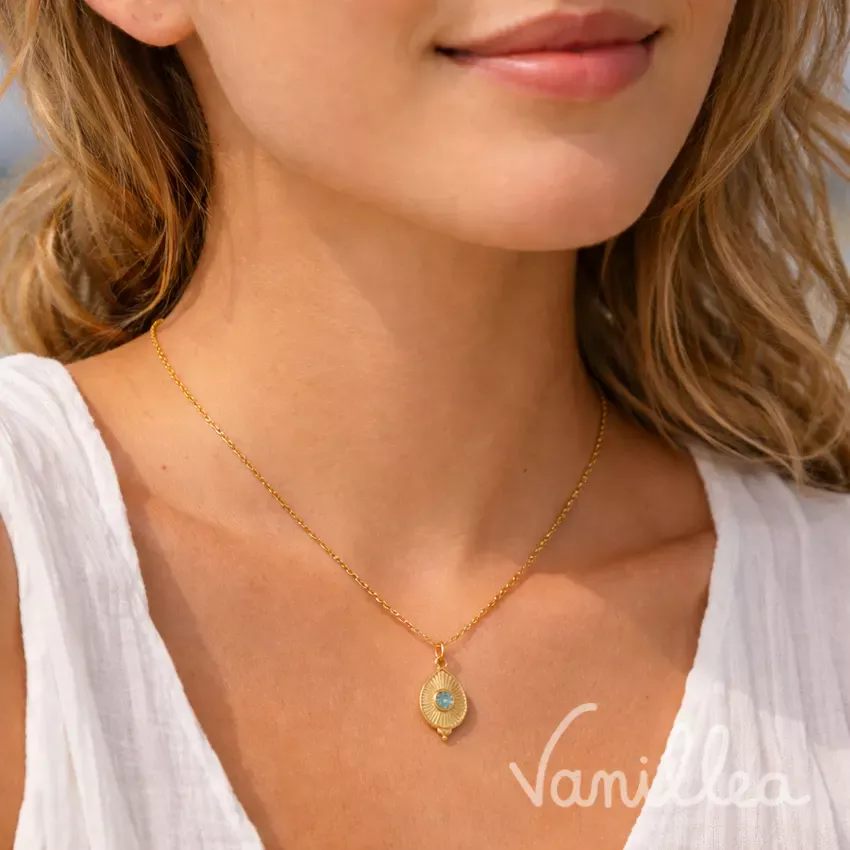 Femme portant un collier fin doré avec pendentif en forme de goutte et cabochon en verre, porté au ras du cou.