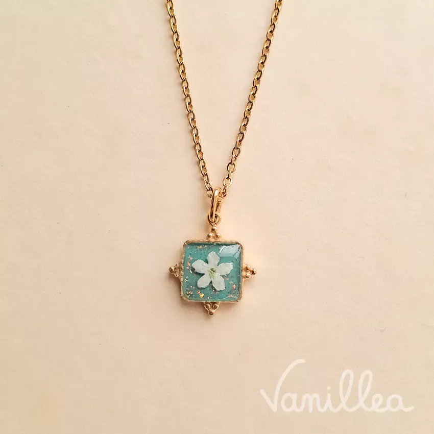 Collier fleur myosotis blanc résine bleu avec pendentif carré doré.